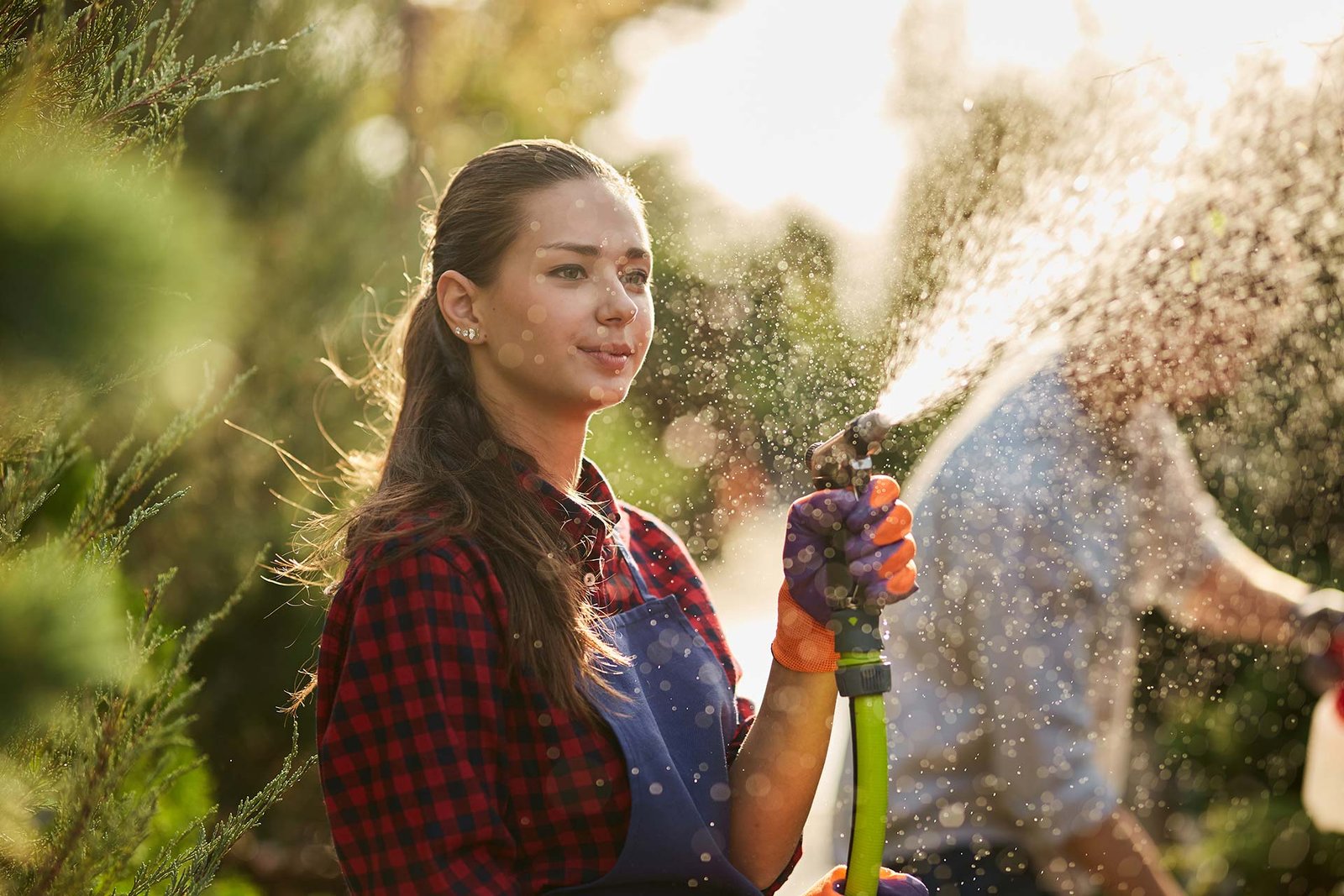 Mujer jardinera con delantal azul utilizando una manguera para regar las plantas